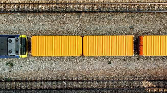 Aerial view of a freight train carrying containers along a rail corridor
