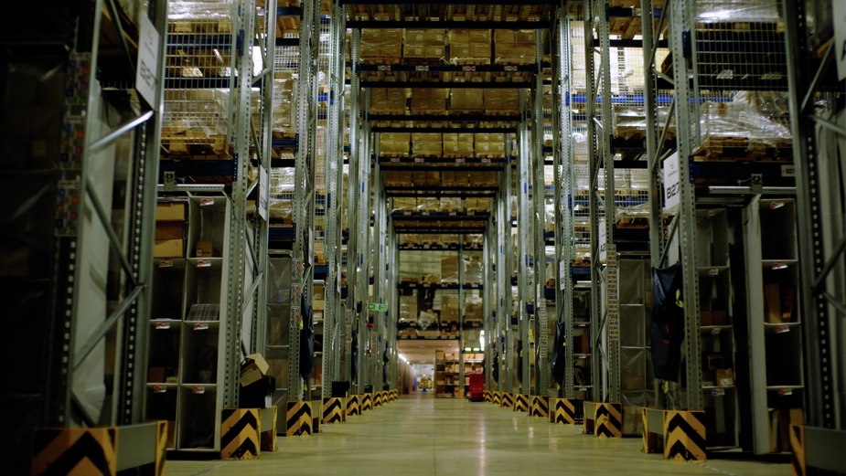 Autonomous mobile robots moving through a warehouse aisle between storage racks, transporting cartons under overhead racking.