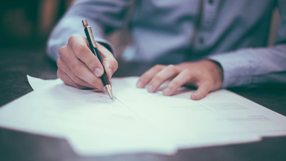 Hand signing a document, representing trade agreements or legal formalities