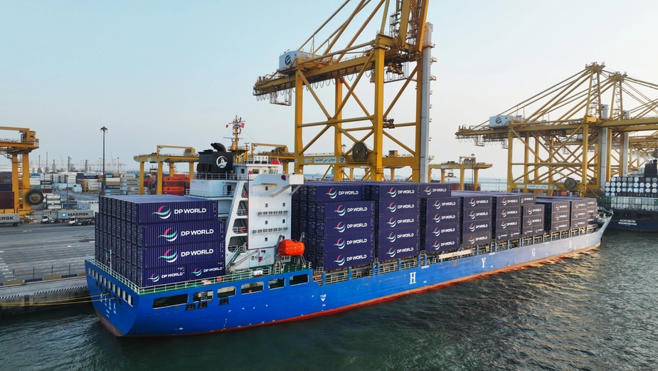 DP World container ship docked at a busy terminal with yellow gantry cranes and cargo containers in the background